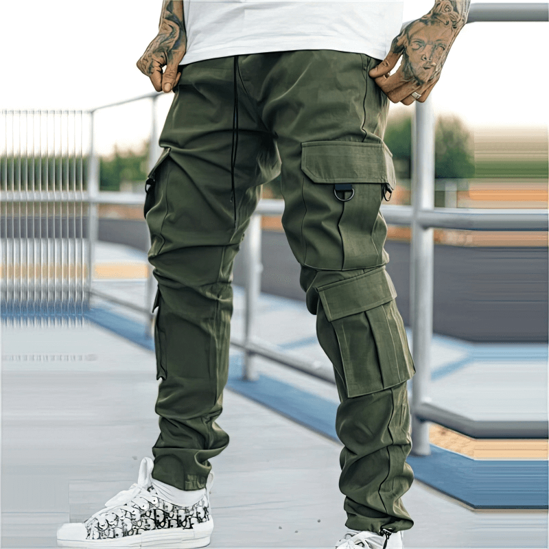 Man wearing green joggers with multiple side pockets, standing by railing in urban setting.